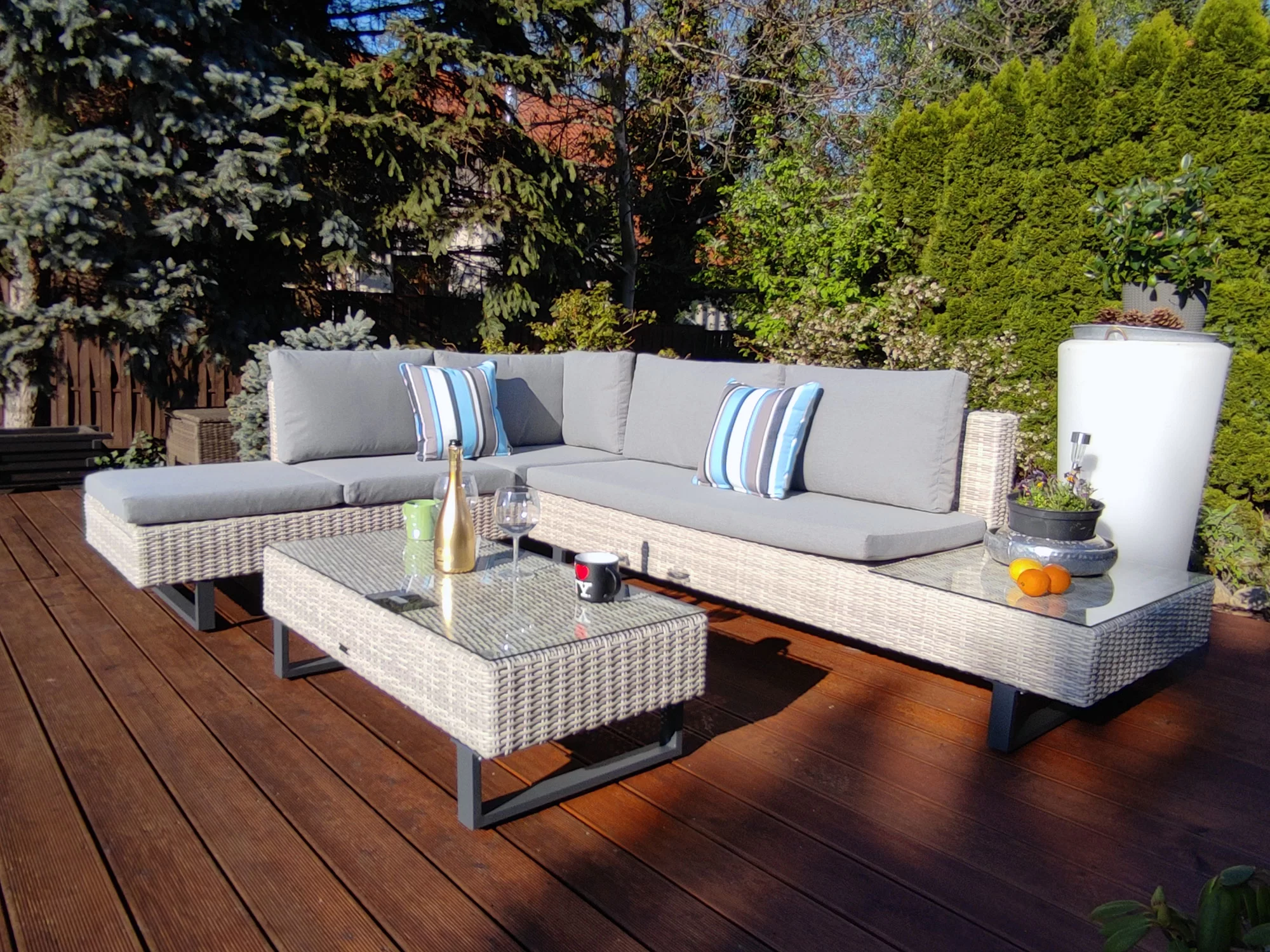 Stolik kawowy PINETO z dekoracjami — butelka, kieliszki, kubek na drewnianym tarasie